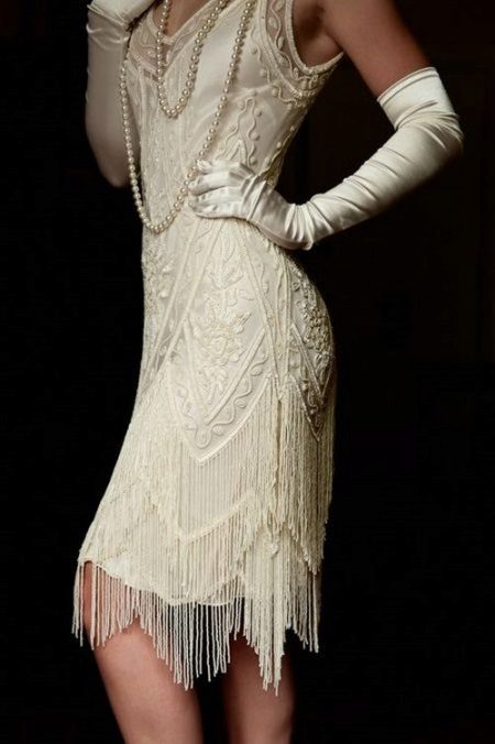 Robe blanche avec un bas asymétrique de la jupe à la manière de Gatsby en combinaison avec des gants et des perles
